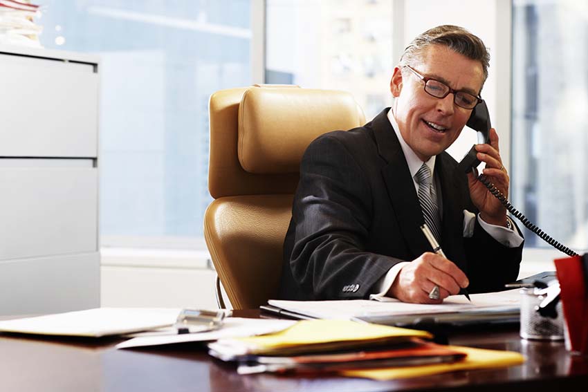 Business professional smiling on the phone and taking notes at a desk. 