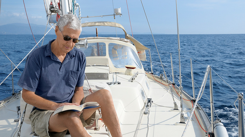 Elderly man sitting on a boat and reading a book