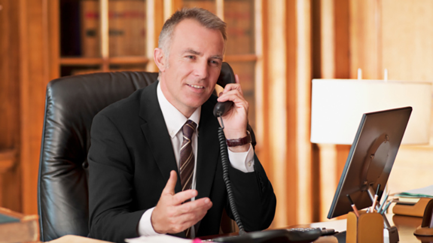 Business man in black suit talks on his phone inside of his office