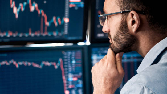 Business professional holds chin while looking at stock graphs