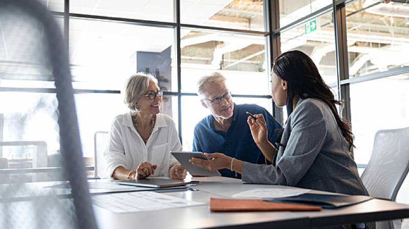 A couple talk with a business woman inside of an office with glass walls