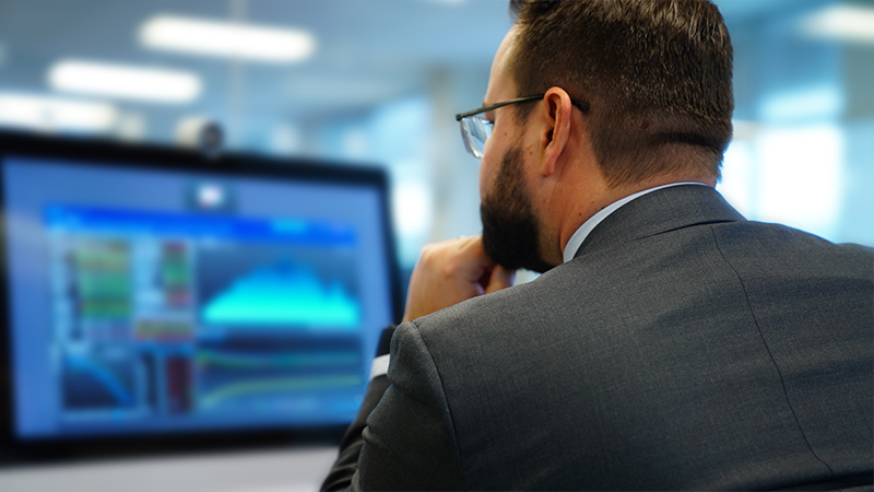 Businessman holds his chin while looking at graphs on a monitor