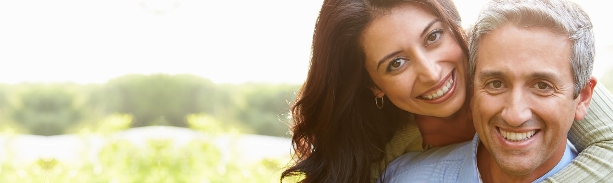 Woman with arm around man outside with green forest behind them