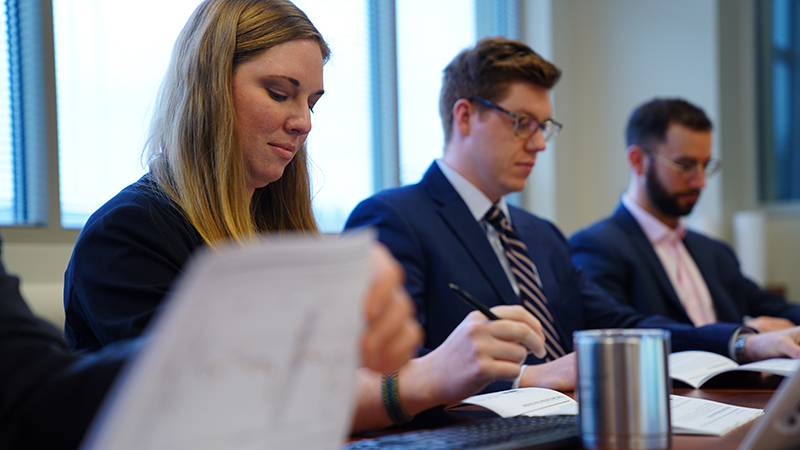 two men and one woman sitting at a table looking at papers