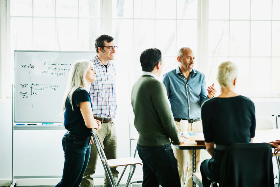Employees stand around a white board discussing the financial market