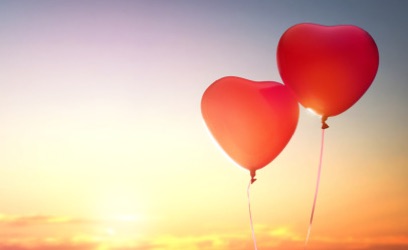 two heart balloons float in front of a setting sun