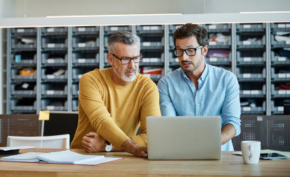 Older man showing younger man something on a laptop