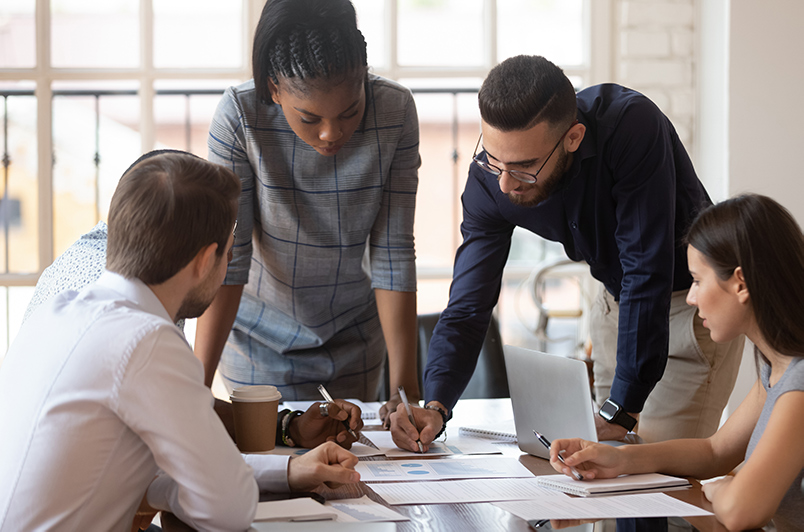 Group of people gather around a table looking over papers that have graphs on them