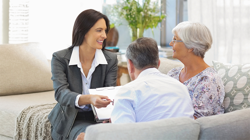 A business woman in a suit working with an older couple in their home