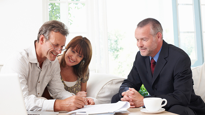 Man wearing dark blue suite with husband and wife signing papers in their living room