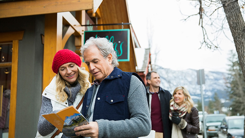 Couple at a ski lodge look at a map of the area outside a ski shop