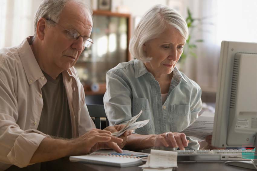 older couple sitting in front of a computer looking at paperwork