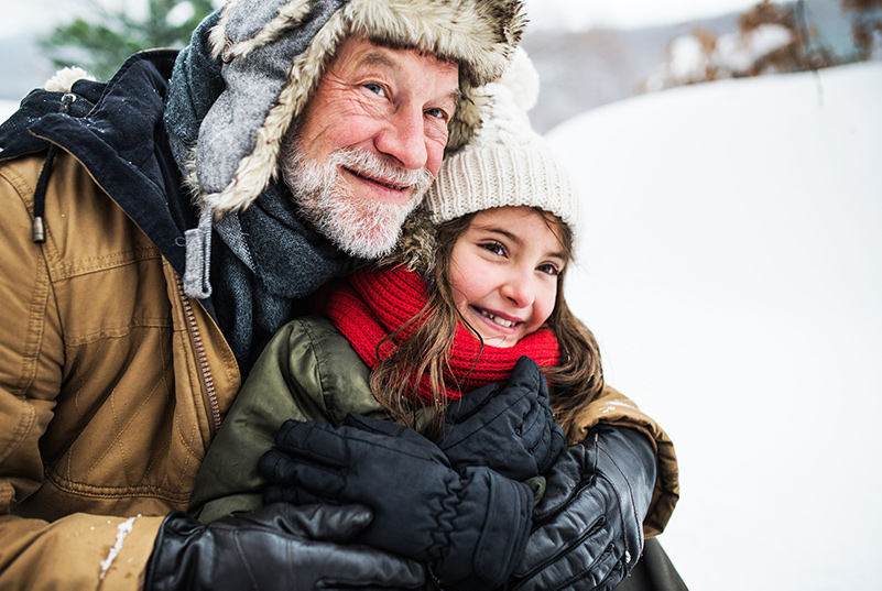 Grandpa holds Granddaughter outside in the show, both wearing winter coats, hats and scarfs