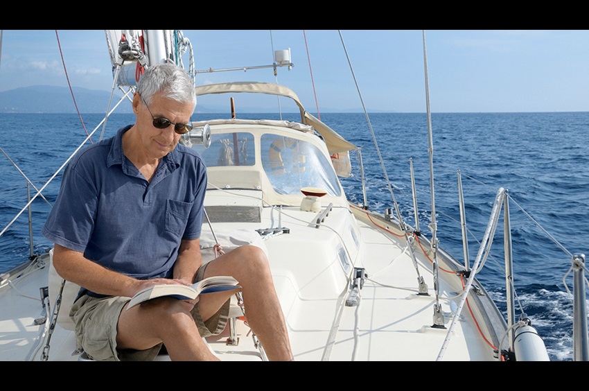 Elderly man sitting on a boat and reading a book