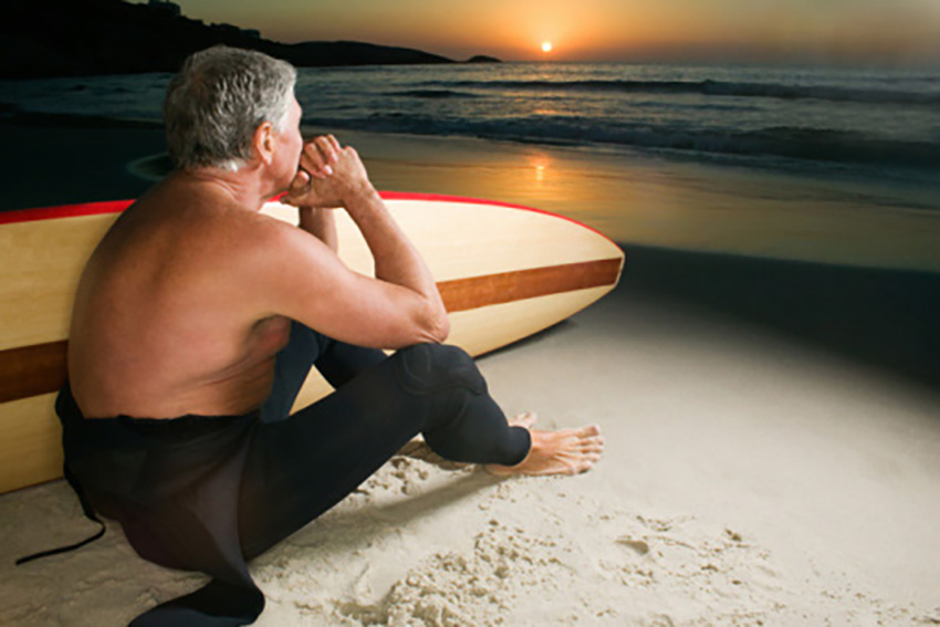 Surfer sitting on the beach with the sunrise