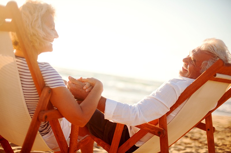 Man and woman holding hands smiling on a beach at sunset