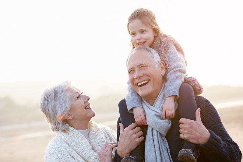 Grandma and Grandpa walking on beach while Granddaughter rides on Grandpas shoulders