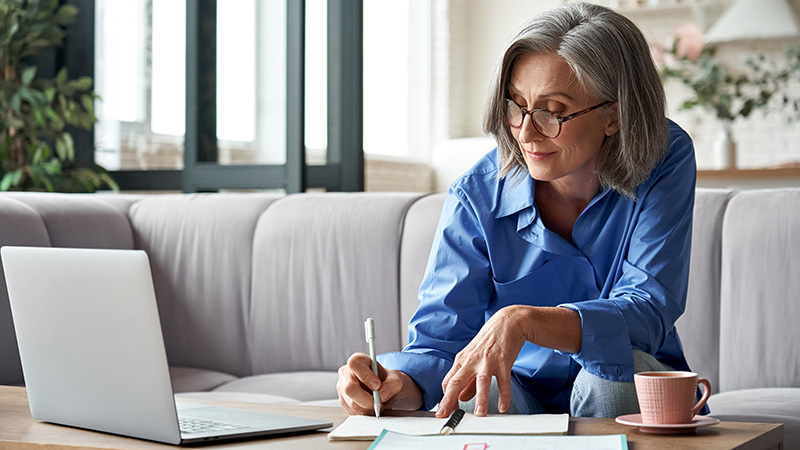 woman looking at her computer while taking notes