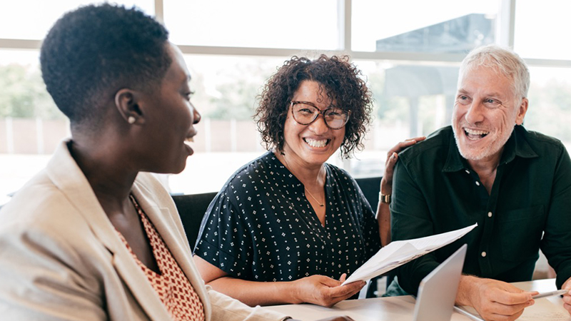 3 people sitting around a desk laughing together