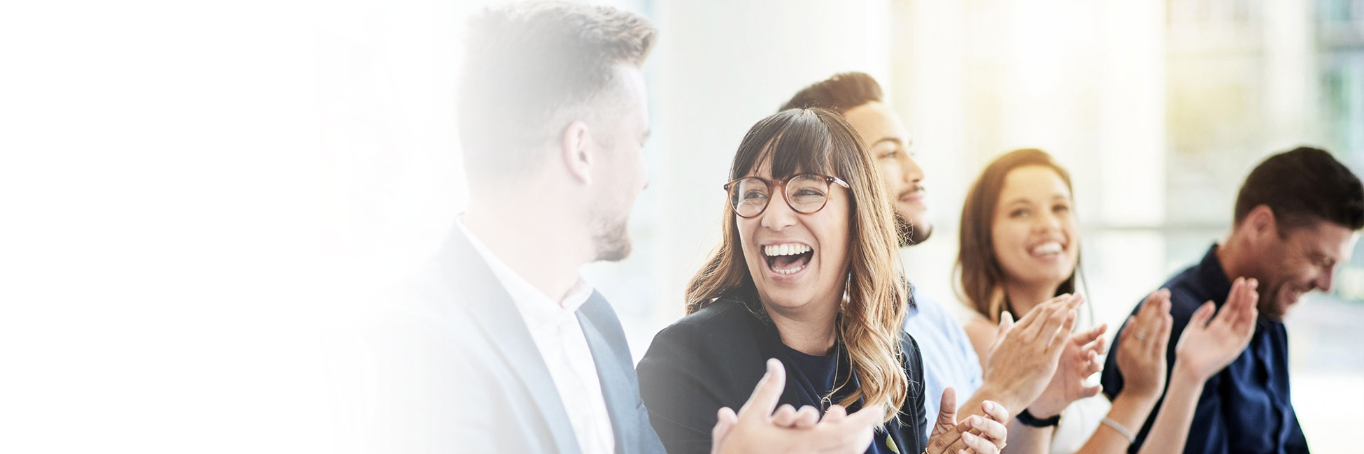Woman in meeting with crowd laughing to the man next to her while everyone claps