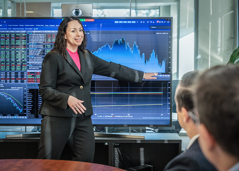 Businesswoman points at a graph and a large TV monitor displaying a graph