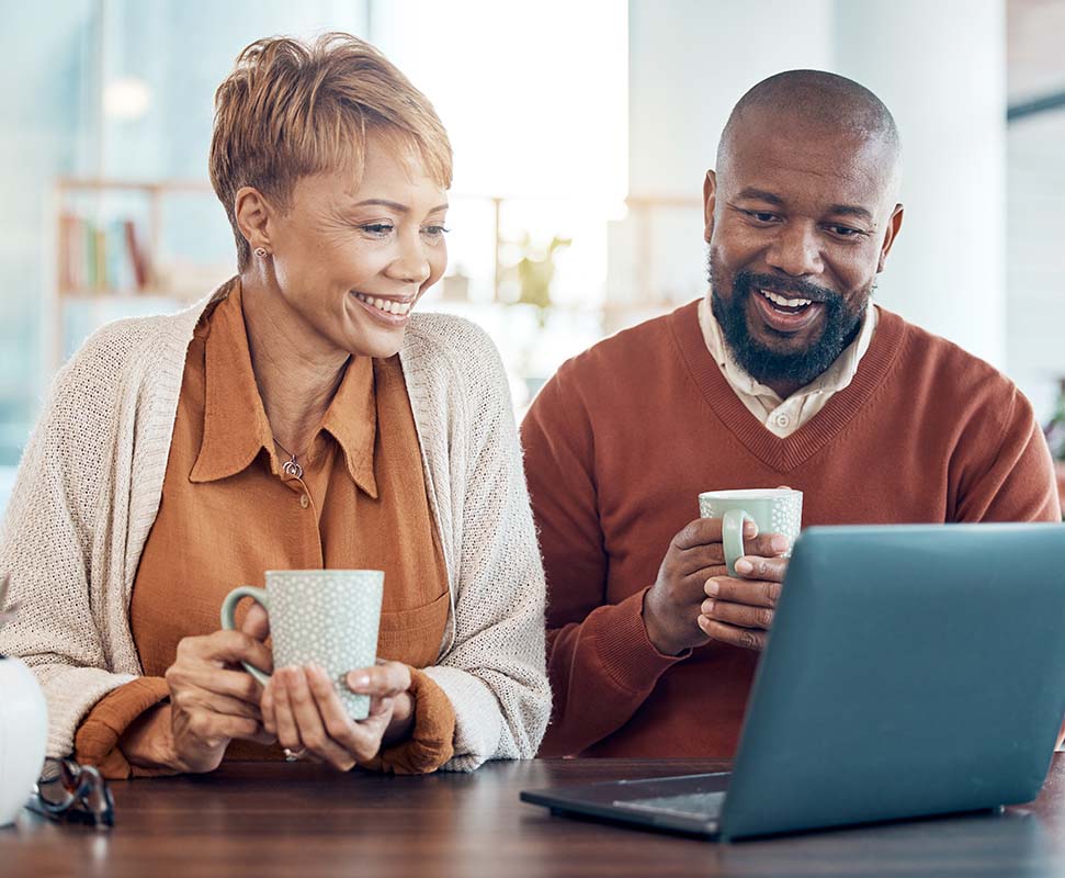 Couple looks over a laptop while drinking coffee