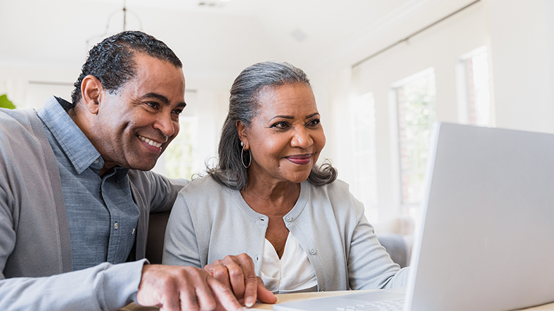 Couple point to some over papers on a desk while looking at a laptop