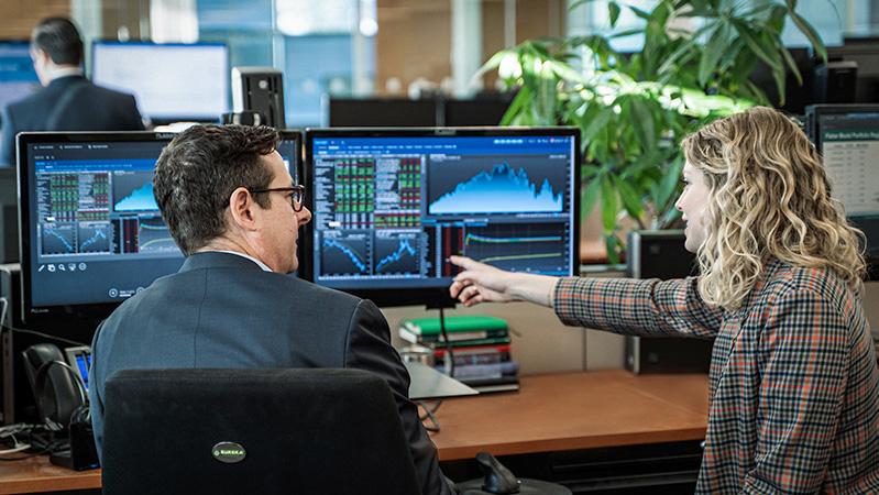 Business woman in sport coat points out a graph on a monitor to a man in a suit