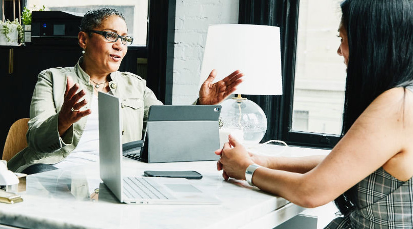 Two people having a discussion around a desk with a tablet